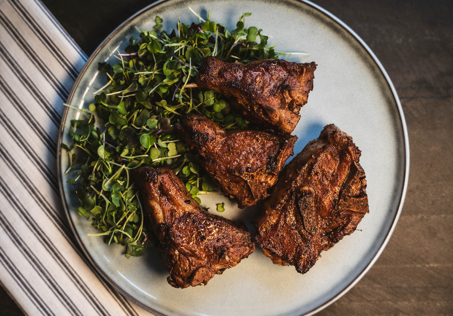 birds eye view of seasoned and cast ironed cook goat chops, plated on a bed of micro greens.